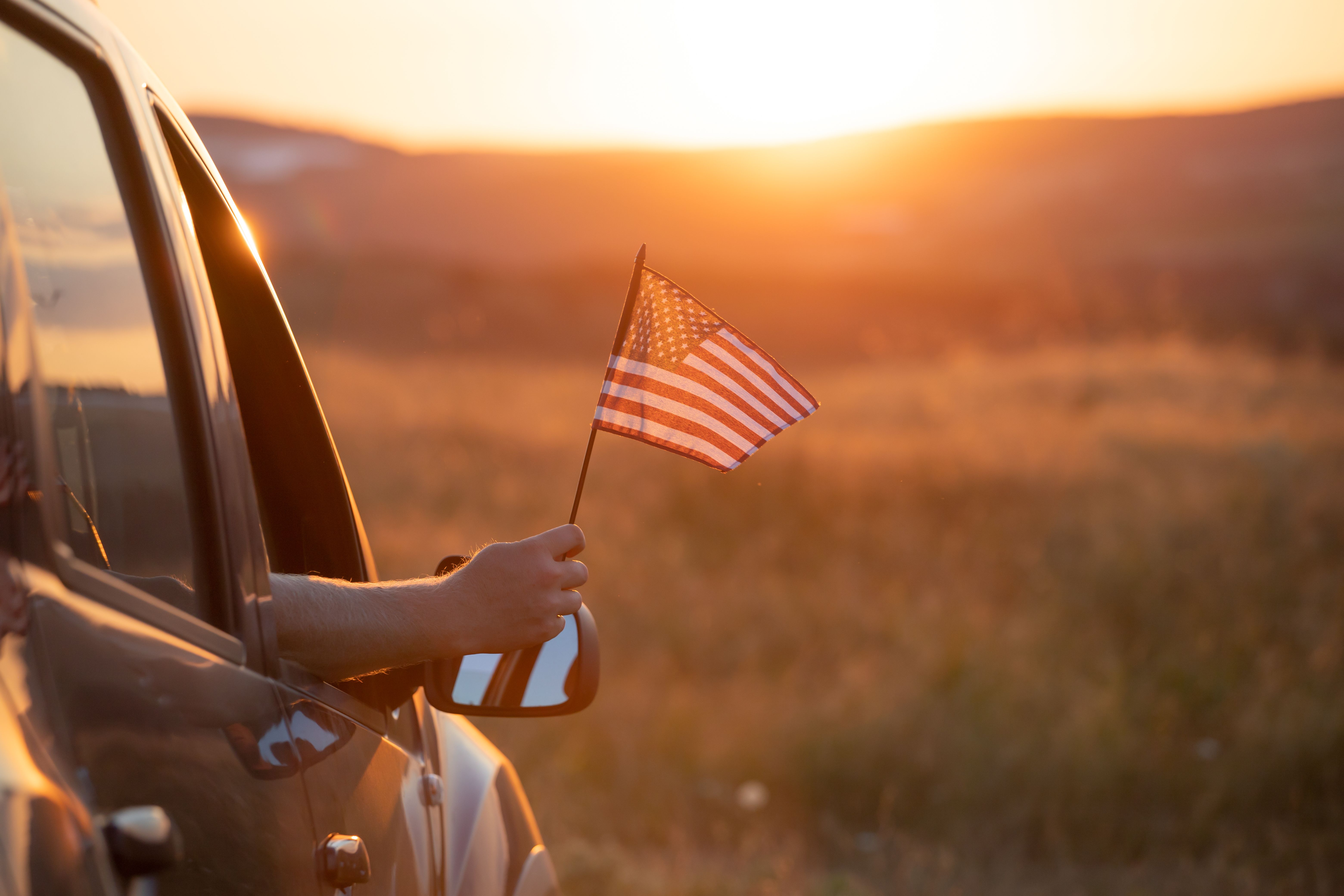 arm-holds-american-flag-from-car-at-sunset.